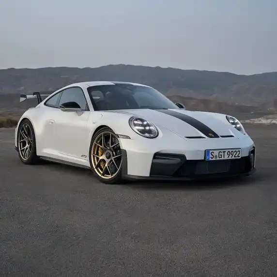 Une voiture de sport Porsche blanche stationnée sur une route ouverte avec un paysage vallonné en arrière-plan.